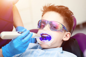 A boy with goggles in the dental chair. Mouth directed lightpolymerization lamp with blue light for sustainable fillings.
