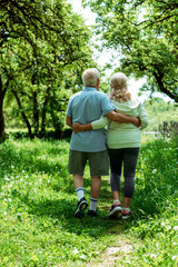 back view of retired man hugging happy senior wife while walking in green park