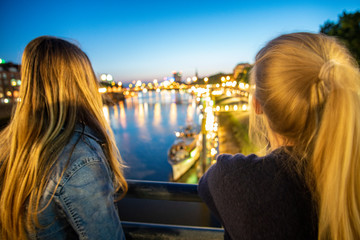 Girls on bridge watching the river by night - obrazy, fototapety, plakaty