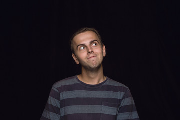 Close up portrait of young man isolated on black studio background. Photoshot of real emotions of male model. Dreaming and smiling, hopeful and happy. Facial expression, human emotions concept.