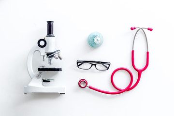 Laboratory desk with stethoscope, pills in test tube and microscope on white background top view