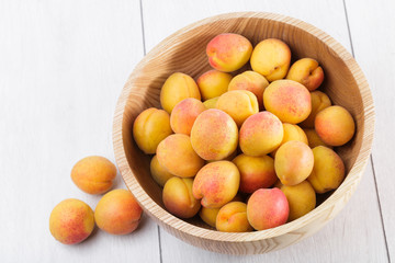 ripe organic apricots fruits in ash tree wooden bowl on a white wooden background