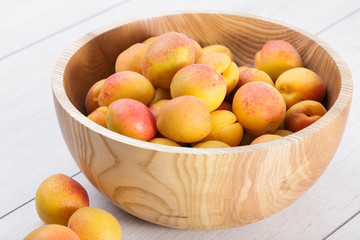 ripe organic apricots fruits in ash tree wooden bowl on a white wooden background