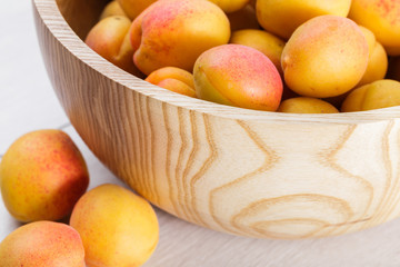 ripe organic apricots fruits in ash tree wooden bowl on a white