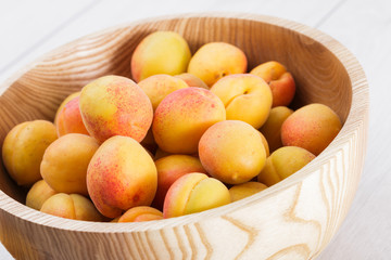 ripe organic apricots fruits in ash tree wooden bowl on a white wooden background