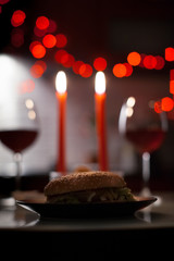 Romantic dinner two glasses of wine and candels, hamburger, nuggets are in the dark with new year lights at the background