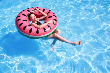 Woman with short hair swimming relaxing in a pool with pink floatie Inflatable doughnut, blue water, chill, tanning under sun.