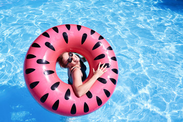 Woman with short hair swimming in a pool, look laughing through pink floatie Inflatable doughnut, blue water. Funny mood. Space for text layout.