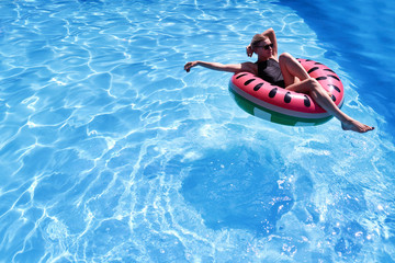 Woman with short hair swimming relaxing in a pool with pink floatie Inflatable doughnut, blue water, chill, tanning. Space for text layout.