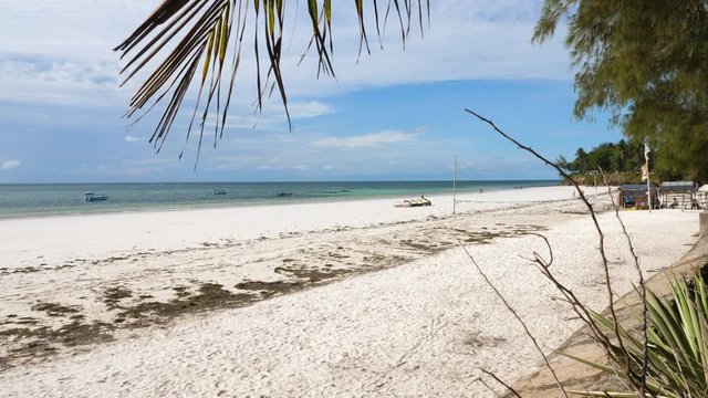 Static, shot a white sand beach, in Mombasa, filmed under a palm tree, boats on the sea, in the background, on a sunny day, at the coast of Kenya, Africa