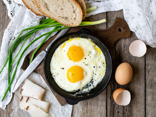 Scrambled eggs in frying pan with pork lard, bread and green feathers onions on old wooden table. National Ukrainian or belorussian food. Breakfast, lunch. Top view, selective focus, rustic style.
