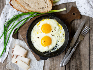 Scrambled eggs in frying pan with pork lard, bread and green feathers onions on old wooden table. National Ukrainian or belorussian food. Breakfast, lunch. Top view, selective focus, rustic style.