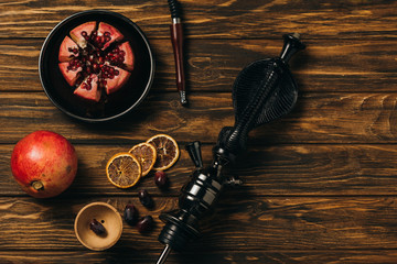 top view of hookah, garnets, grapes and dried cut oranges on wooden surface