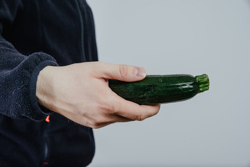 The man is holding a zucchini in his hand. The concept of collecting vegetables and fruits. Using spices, vegetables for preparing meals.