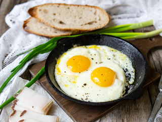 Scrambled eggs in frying pan with pork lard, bread and green feathers onions on old wooden table. National Ukrainian or belorussian food. Breakfast, lunch. Close up, selective focus, rustic style.