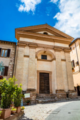 Fototapeta na wymiar June 1, 2019 - Spello, Perugia, Umbria, Italy - A church with a tympanum and a wooden door in the historic center.