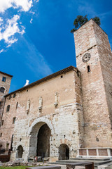 Fototapeta premium The Roman consular door, with the tower and the clock. One of the accesses to the city walls. Three statues above the arch. In Spello, province of Perugia, Umbria, Italy.