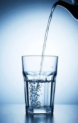 Pouring water into glass on blue background.