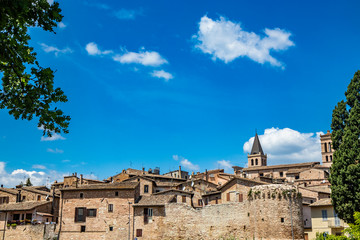 Fototapeta premium A view of the medieval village of Spello, with stone and brick houses, city walls. The blue sky in the summer. In the province of Perugia, Umbria, Italy.