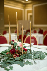 The wedding table setting is decorated with fresh flowers in a brass bowl and golden candles in brass candlesticks. Wedding floristry. Banquet table for guests. Bouquet with dahlias and eucalyptus