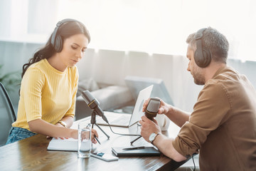 two serious radio hosts talking while sitting at workplace in radio studio