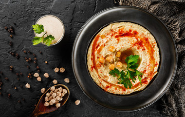 Chickpeas hummus with olive oil, paprika in a plate over dark stone background. Healthy vegan food, clean eating, dieting, top view
