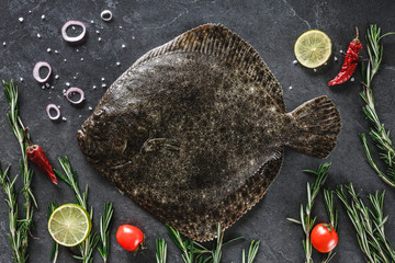 Raw whole flounder fish with rosemary, onions and spices on dark stone background. Creative layout...