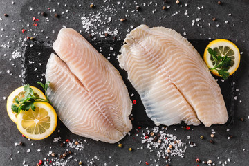 Fresh raw fillet white fish Pangasius with spices and lemon on dark stone background.  Seafood, top view, flat lay, copy space - obrazy, fototapety, plakaty