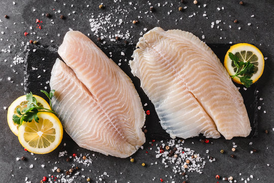 Fresh raw fillet white fish Pangasius with spices and lemon on dark stone background.  Seafood, top view, flat lay, copy space