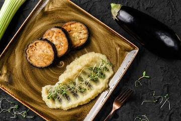 Celery puree with sprouts and grilled eggplant in plate over dark background. Healthy vegan food, clean eating, dieting, top view