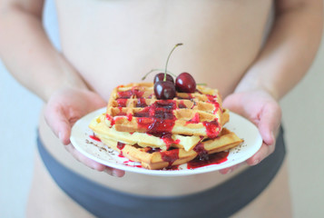 delicious Belgian waffles with cherry syrup and chocolate chips on a white plate with a juicy cherry on the top against the background of a seductive naked female body