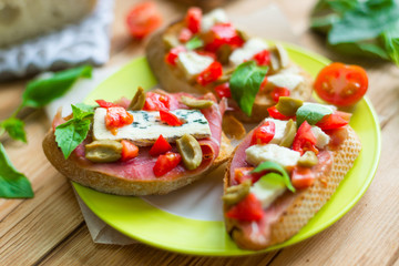 Traditional Italian bruschetta with blue cheese, feta, tomatoes, basil leaves, jamon on a wooden background.