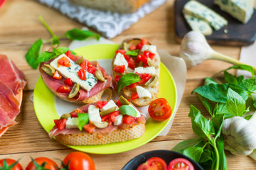 Traditional Italian bruschetta with blue cheese, feta, tomatoes, basil leaves, jamon on a wooden background.
