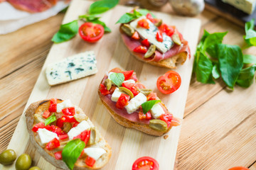 Traditional Italian bruschetta with blue cheese, feta, tomatoes, basil leaves, jamon on a wooden background.
