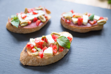 Traditional Italian bruschetta with blue cheese, feta, tomatoes, basil leaves, jamon on black stone...