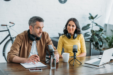 pretty radio host looking at camera while sitting at workplace near colleague