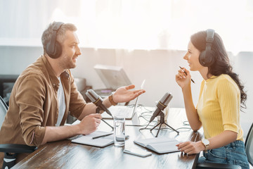 two radio hosts in headphones talking while recording podcast in radio studio - obrazy, fototapety, plakaty