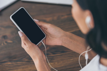 cropped view of woman in earphones holding smartphone with blank screen