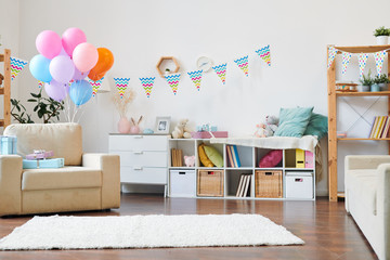 Bunch of colorful balloons and stack of giftboxes on armchair in the living-room