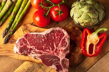 Fresh raw piece of marbled beef steak with fresh vegetables and Italian spaghetti, on a roasting board, on a wooden background.