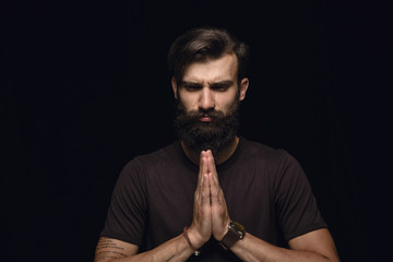Close up portrait of young man isolated on black studio background. Photoshot of real emotions of male model. Praying and crying, looks sad and hopeful. Facial expression, human emotions concept.
