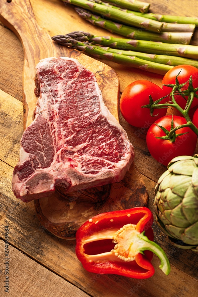 Wall mural Juicy fresh piece of marbled beef steak with vegetables for grilling. Culinary background, recipe book, taste food, Steak cooking. With space, vertical photo