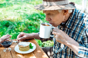 senior man in straw hat drinking tea near sweet and tasty pancakes