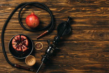 top view of hookah, garnets and dried cut orange on wooden surface