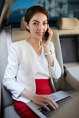 Portrait of successful businesswoman looking at camera and speaking by phone in back seat of luxury car, copy space