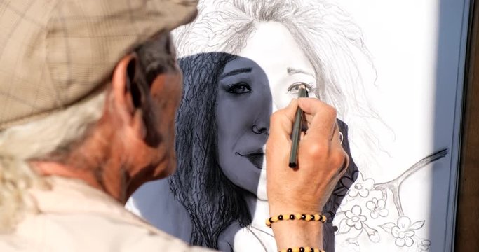 Skilled senior man painting in a public square in Madrid, Spain. Creative Spanish artist drawing on the street. Person and creativity. Detail of hand holding pencil