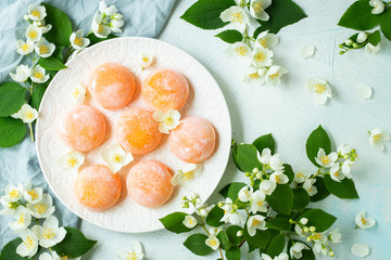 Multi-colored Japanese ice cream Mochi in rice dough and Jasmine flowers on a concrete blue background. Traditional Japanese dessert on a white plate. Top view. Flat lay