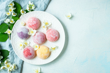 Multi-colored Japanese ice cream Mochi in rice dough and Jasmine flowers on a concrete blue...