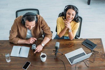 overhead view of two cheerful radio hosts recording podcast while sitting at wooden table