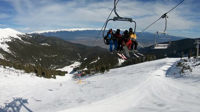 Ski lift transporting skiers, snowboarders at top of world cup ski piste Tomba in Bansko, Bulgaria with view of Banderitsa at background